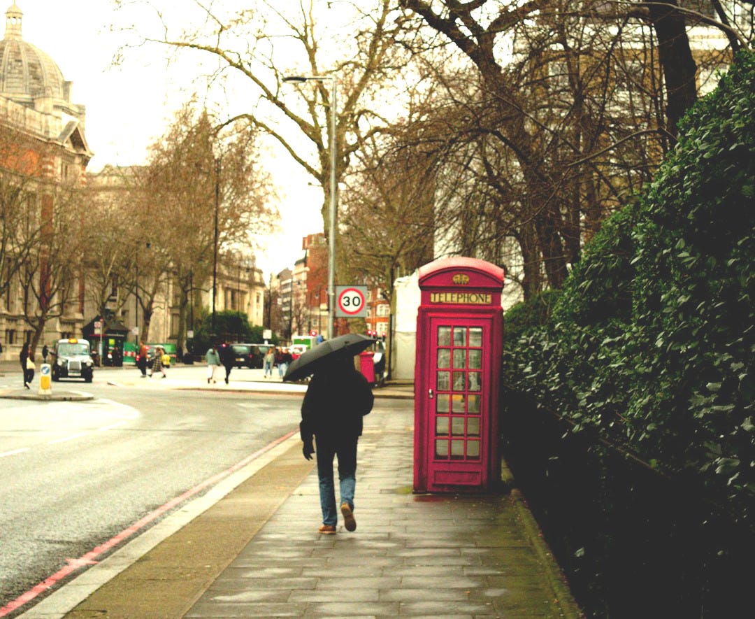 A person walking down a sidewalk next to a red phone booth