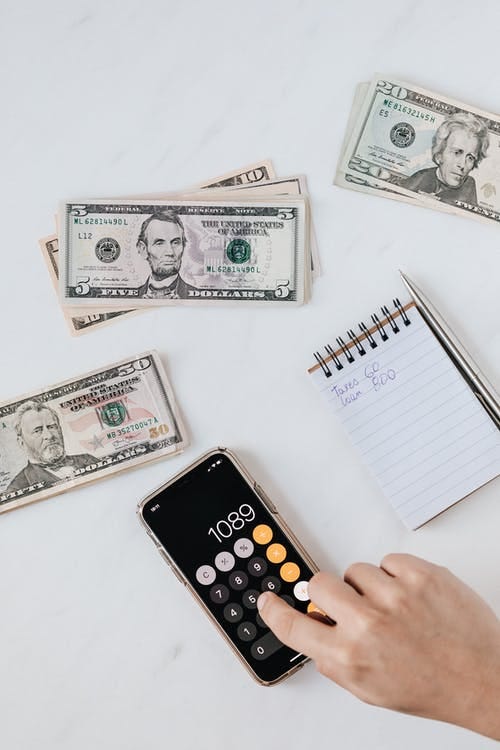 Free Crop anonymous person calculating profit on smartphone calculator near banknotes Stock Photo