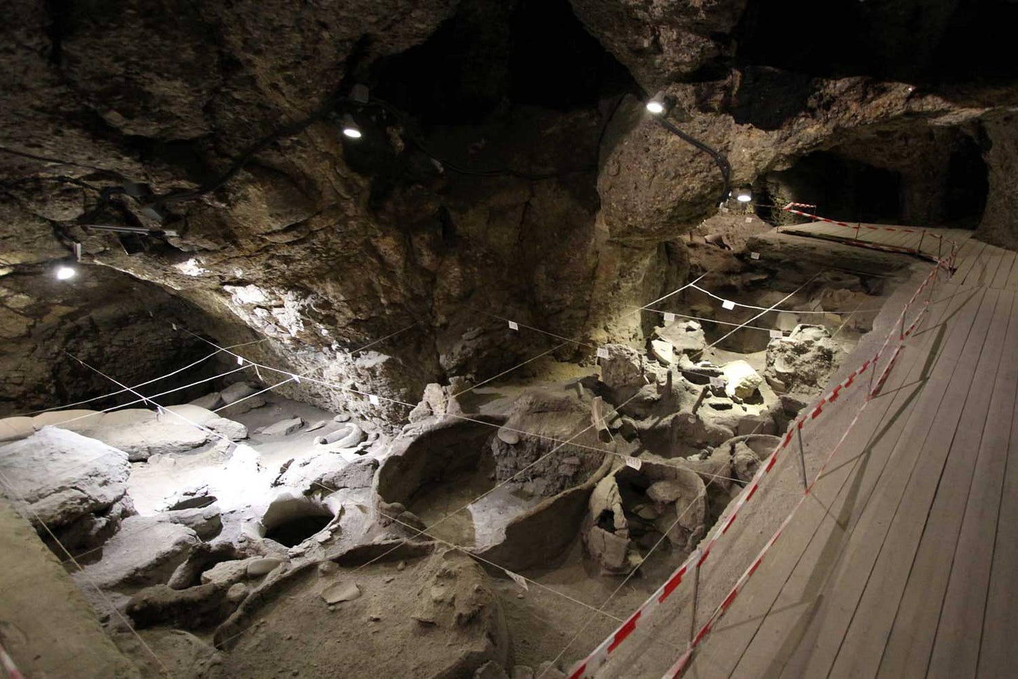 An archaeological excavation area with exposed storage pits inside of a cave, with a boardwalk flanking it at right. An archaeological excavation area with exposed storage pits inside of a cave, with a boardwalk flanking it at right.