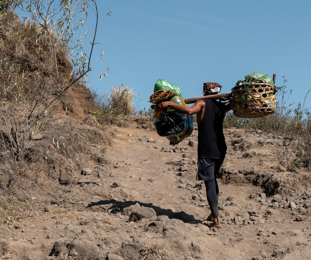 A man walking down a dirt road carrying bags