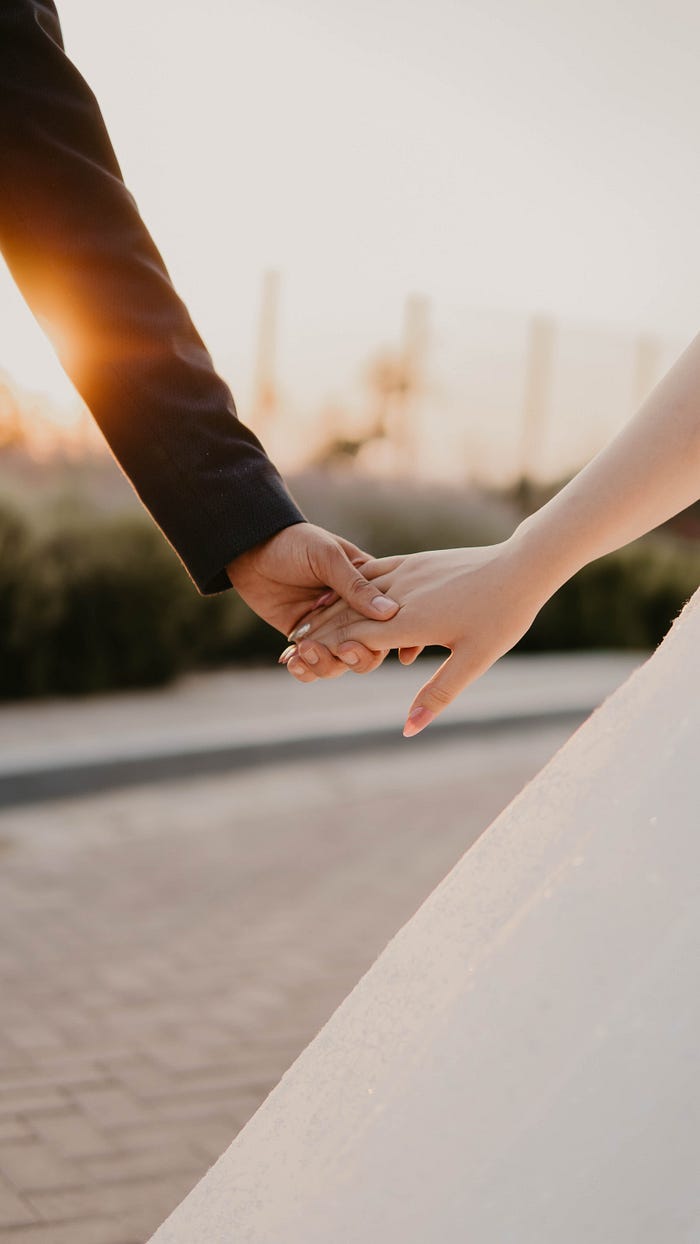 A bride and groom hold hands in a wedding photo.