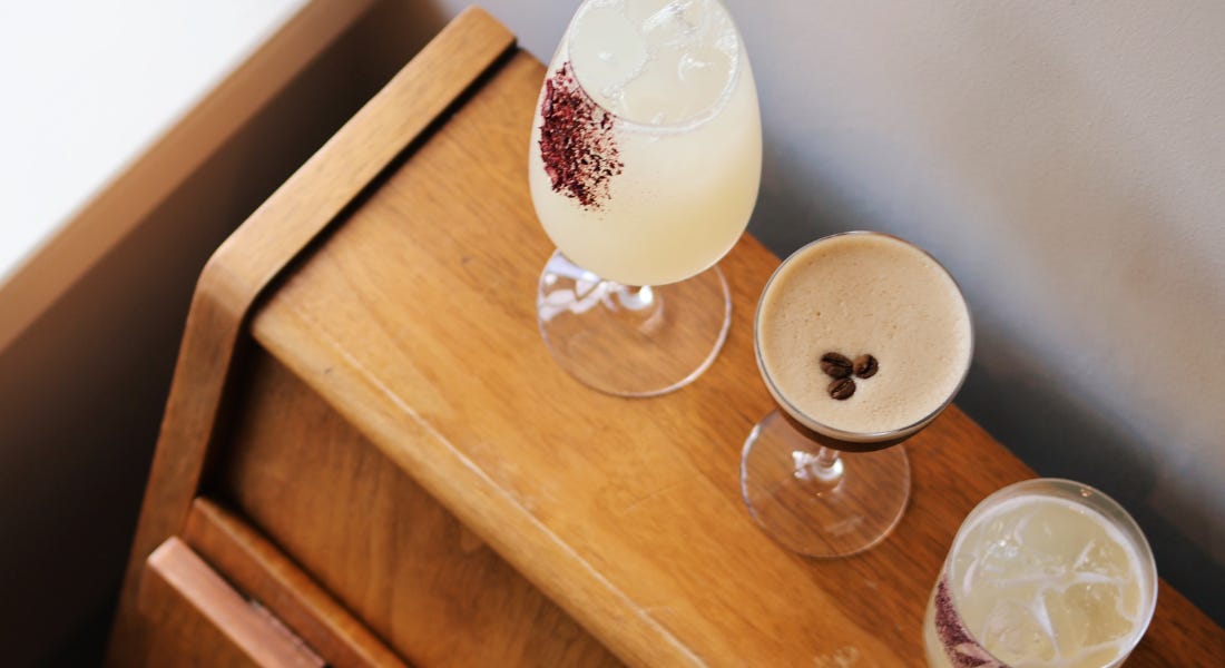 Three cocktail glasses on top of a light wooden piano