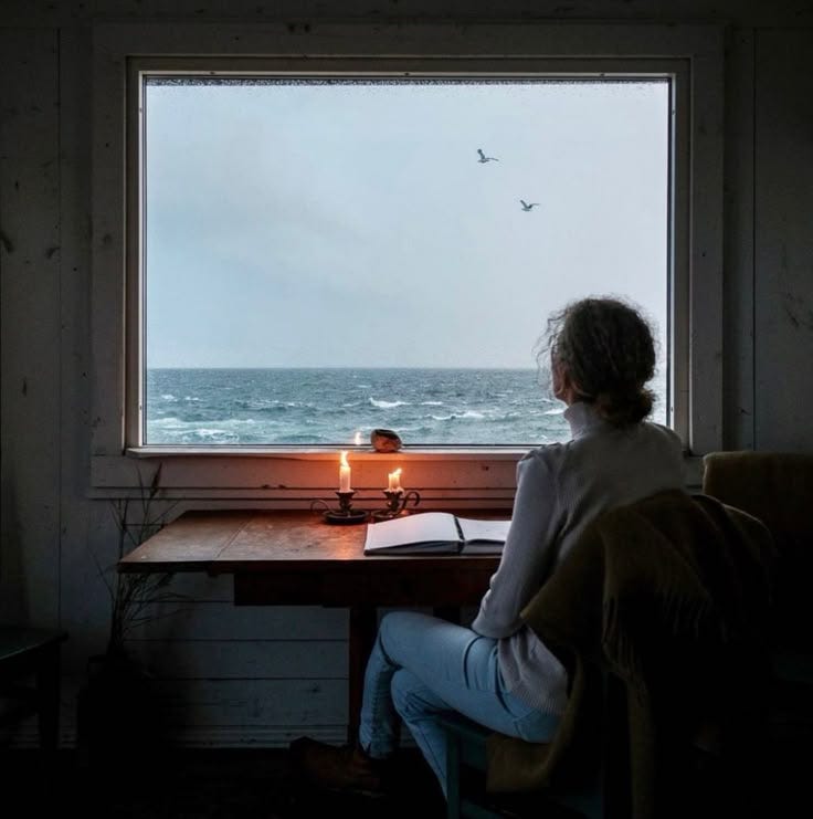 This may contain: a woman sitting at a desk in front of a window with a lit candle on it