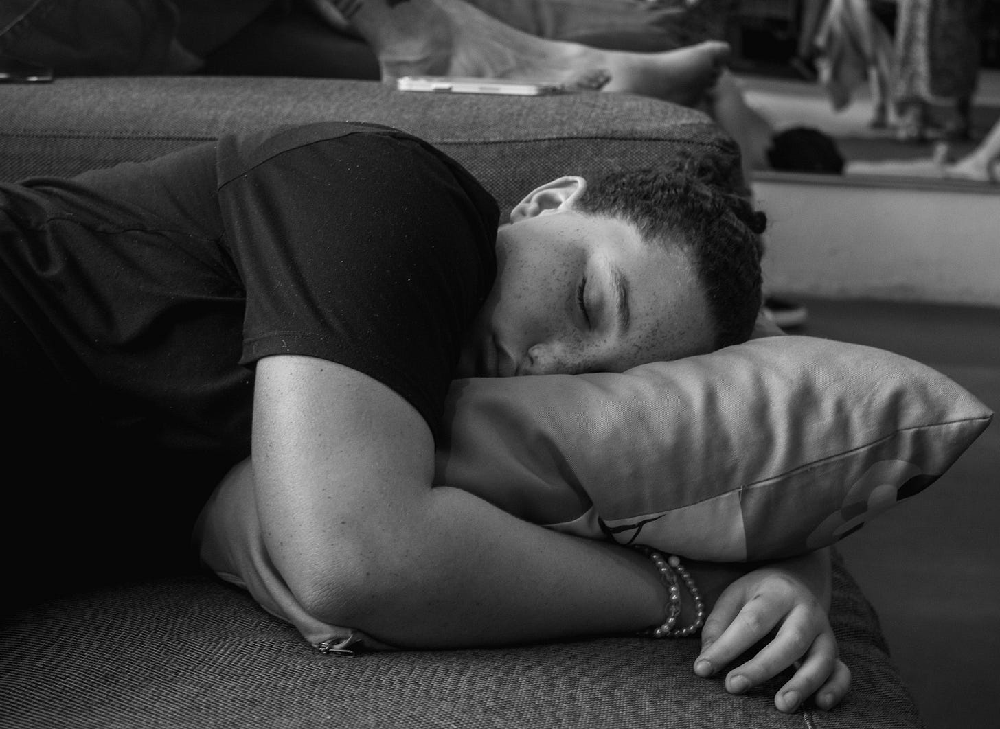 Black-and-white close-up of a sleeping person curled on a couch with a pillow, in a calm indoor setting. Black-and-white close-up of a sleeping person curled on a couch with a pillow, in a calm indoor setting.