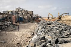 A row of houses right next to a beach and about 3 metres away a wall of rocks piled on top of each other A row of houses right next to a beach and about 3 metres away a wall of rocks piled on top of each other