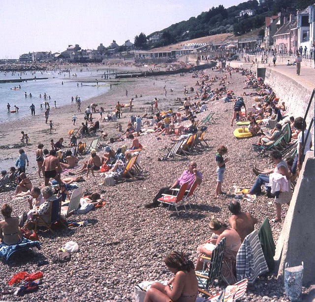 Photograph of a very crowded beach during the 1976 UK heatwave. People are sat on towels or deck chairs sunbathing, or paddling in th sea. Photograph of a very crowded beach during the 1976 UK heatwave. People are sat on towels or deck chairs sunbathing, or paddling in th sea.