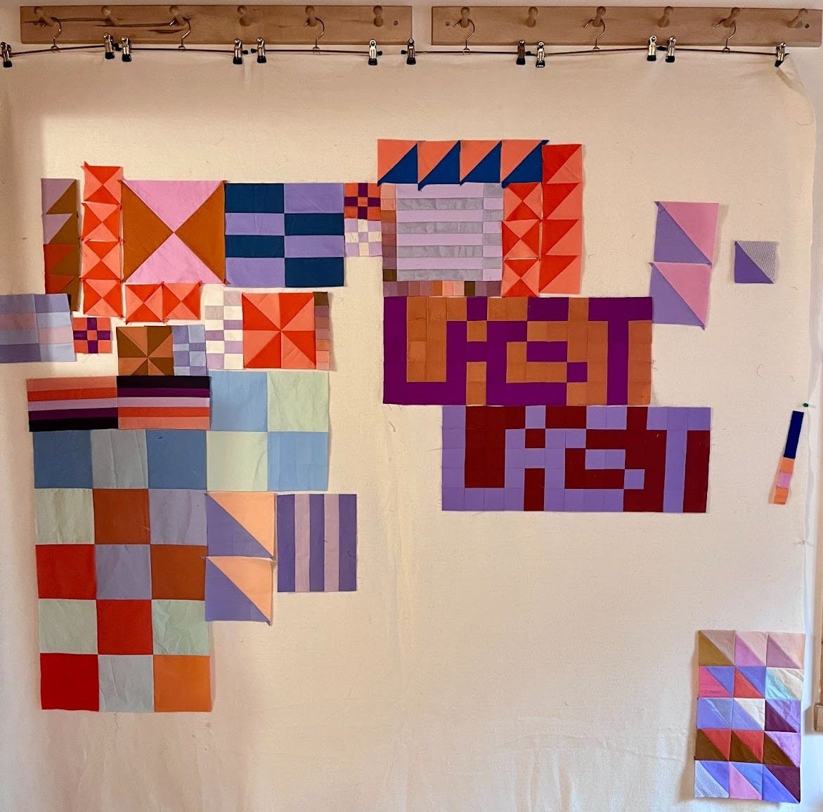 Pieces of brightly colored fabric hang from a cotton batting design wall. The fabric ‘sticks’ to the batting, so the pieces can be moved around to try different compositions. 