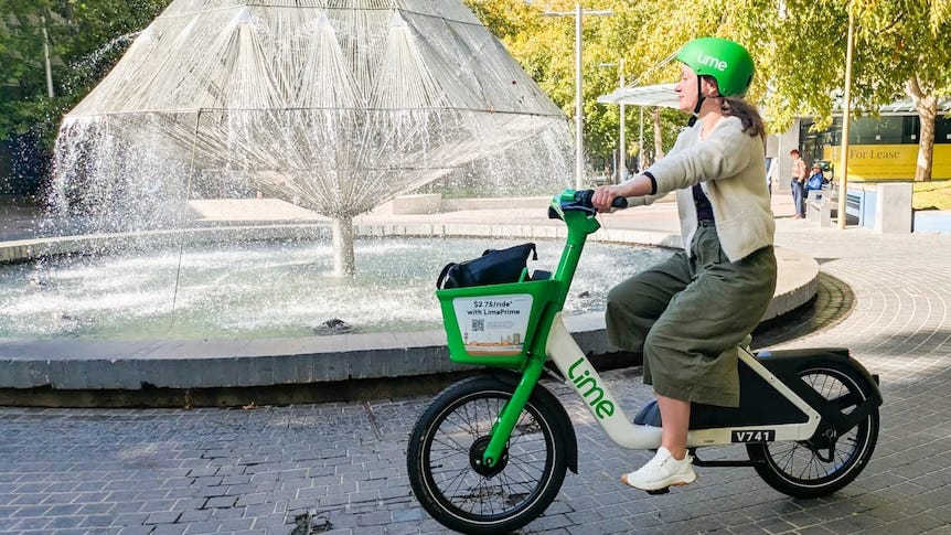 A person rides a green Lime bike near a fountain in an urban space. A person rides a green Lime bike near a fountain in an urban space.