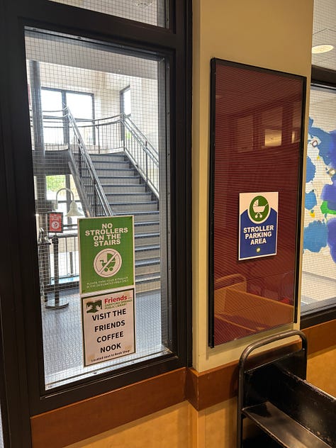 Pictures inside the Saratoga Springs library include the walls erected for elevator reapair and signs reminding people not to bring strollers on stairs and where to get coffe.