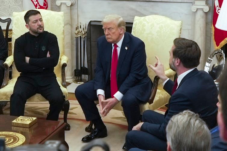 Three men sit in discussion, one gesturing with his hand pointing upwards. Three men sit in discussion, one gesturing with his hand pointing upwards.