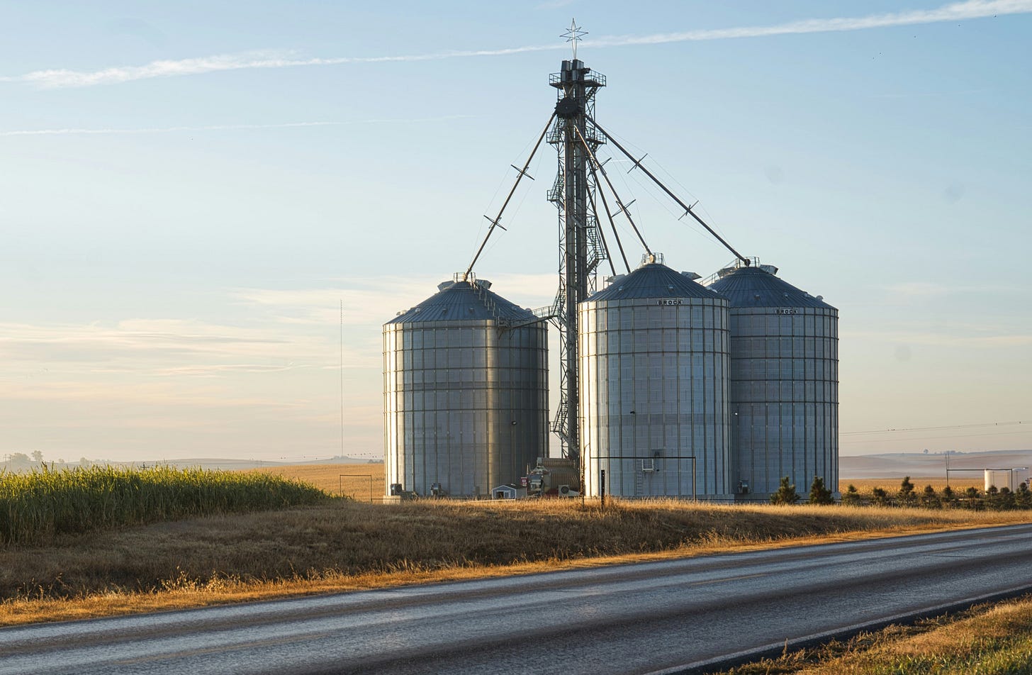 Three metal silos sit among farm fields