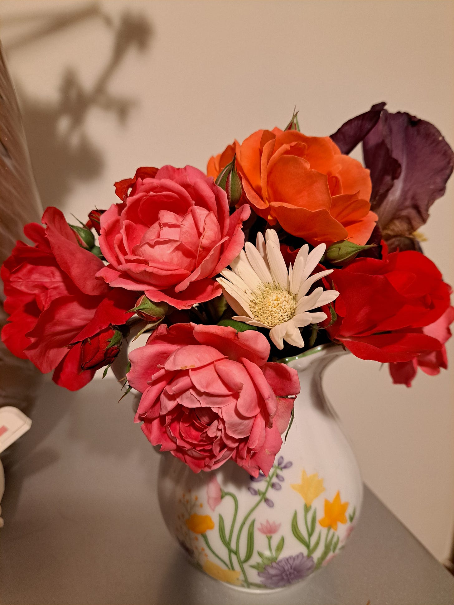 A picture of a floral arrangement with roses, peonies, and other flowers, in a ceramic vase.