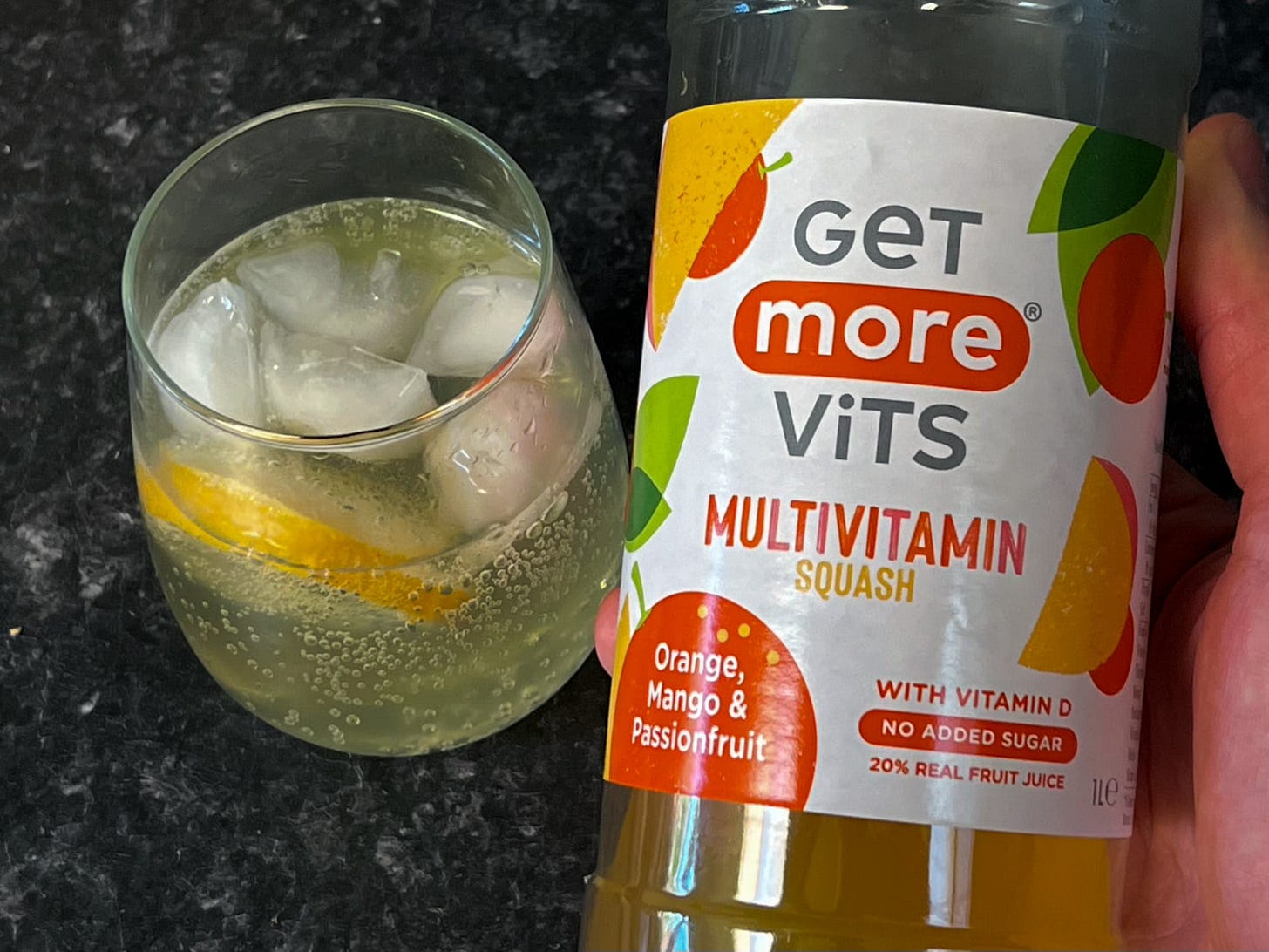 A bottle of cordial being held next to a delicious looking iced drink.