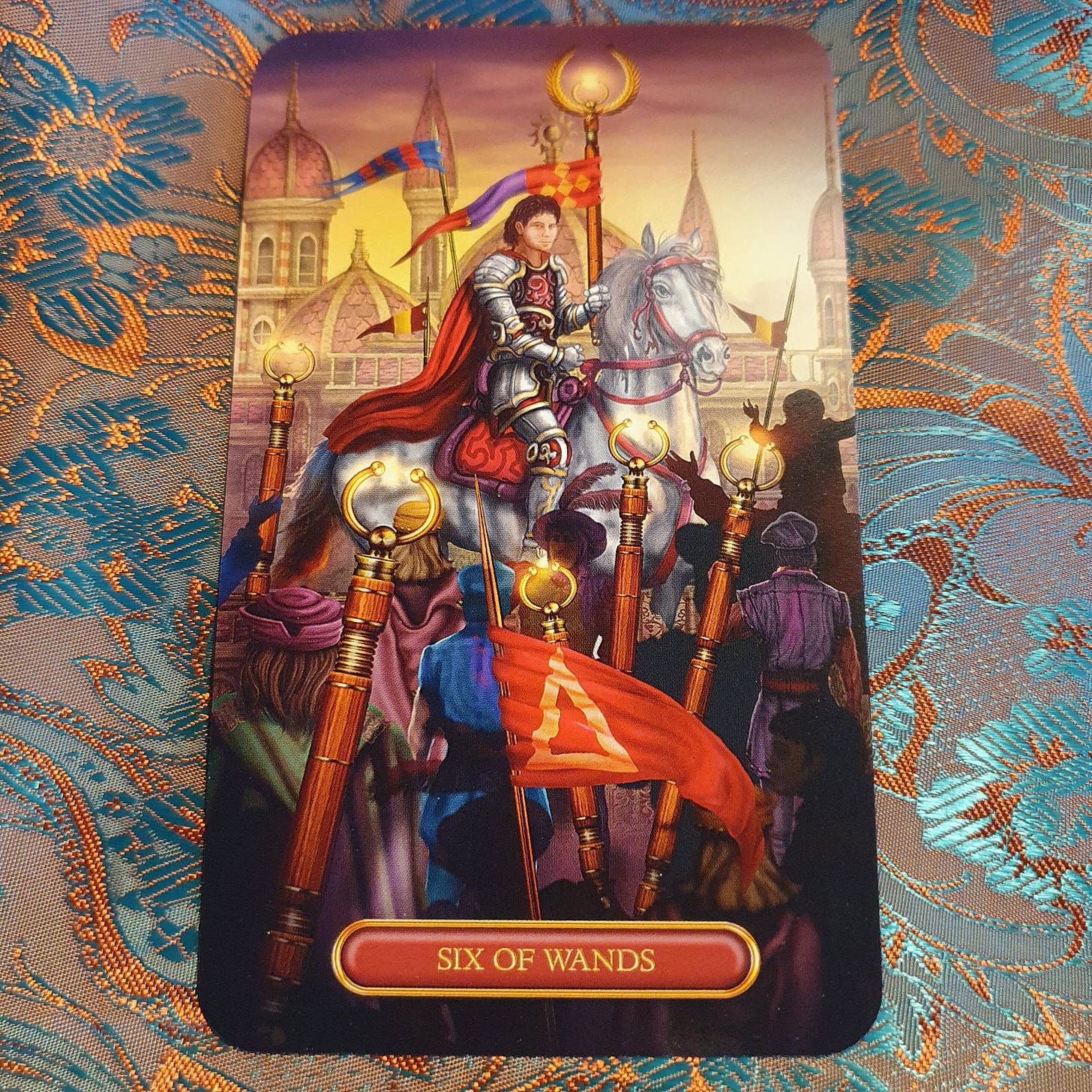 The Six of Wands on an orange and teal patterned background The Six of Wands on an orange and teal patterned background