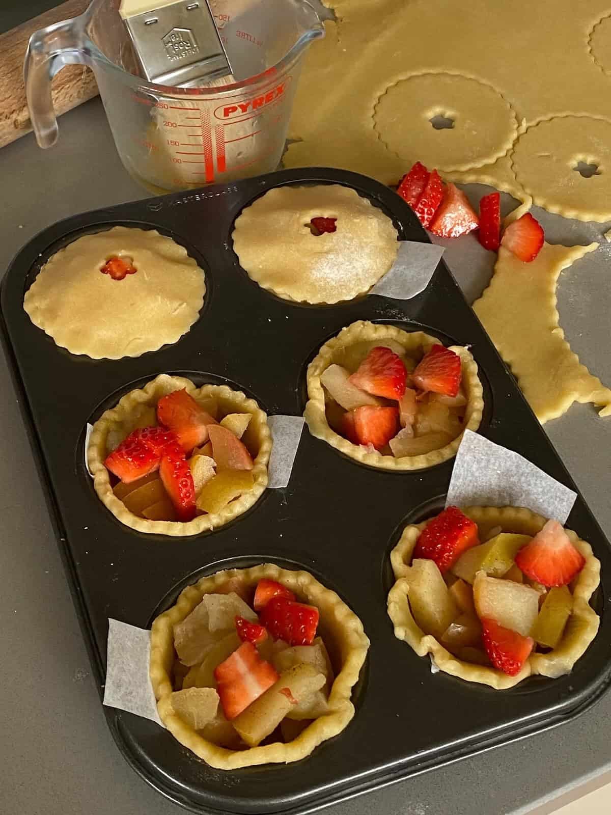 Tray of unbaked small strawberry and apple tarts.