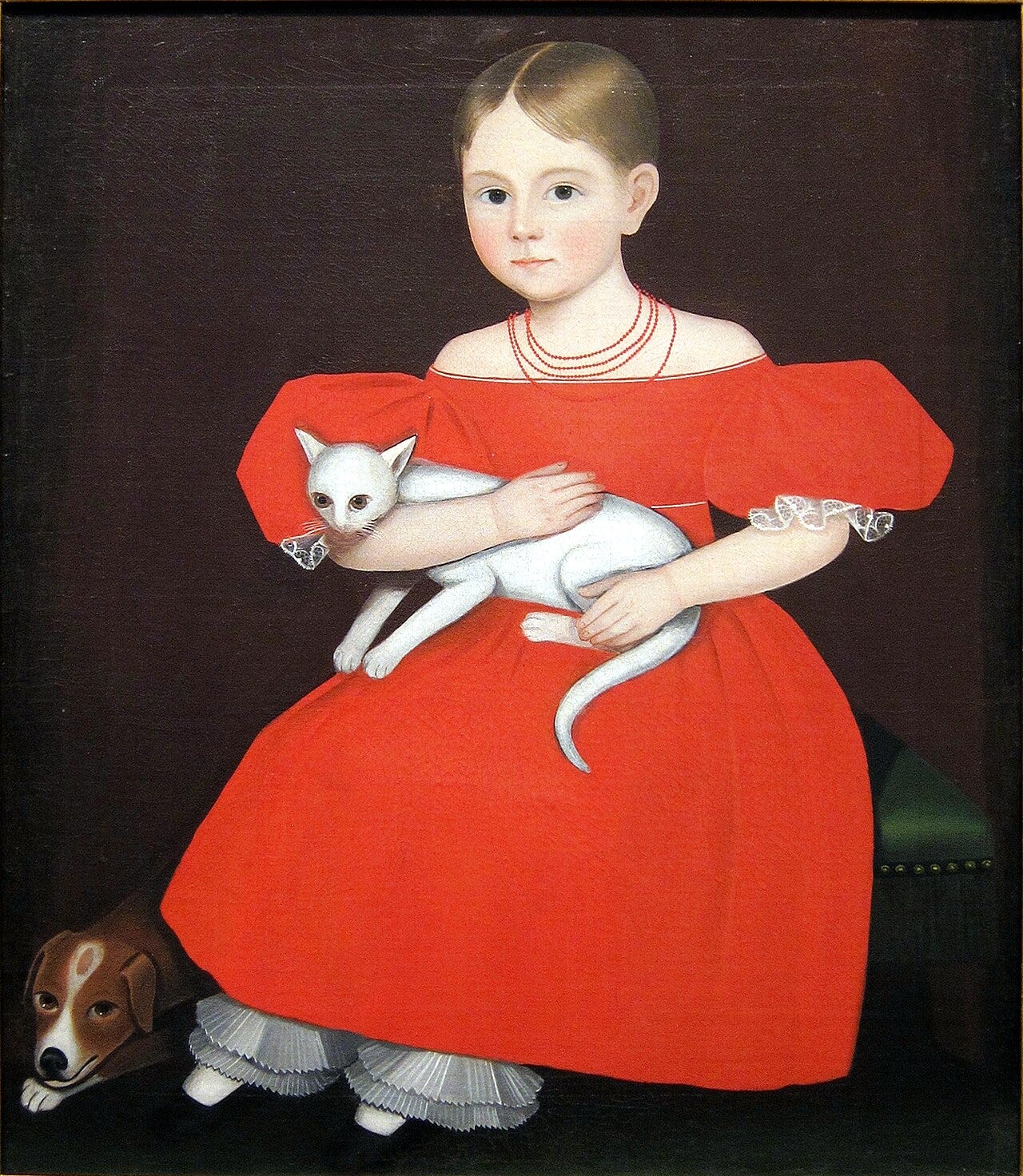 A solemn child in a bright red dress holds a white cat while a small dog sits below A solemn child in a bright red dress holds a white cat while a small dog sits below