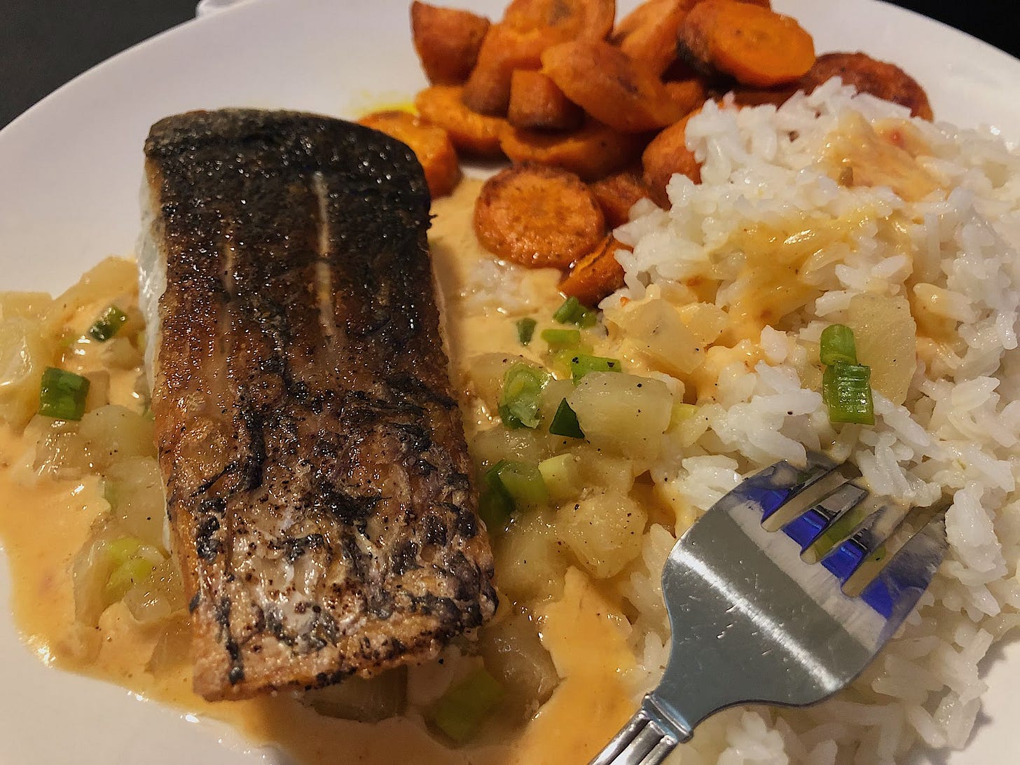 A picture of seared barramundi over pineapple scallion salsa, coconut rice, and a side of roasted carrots.