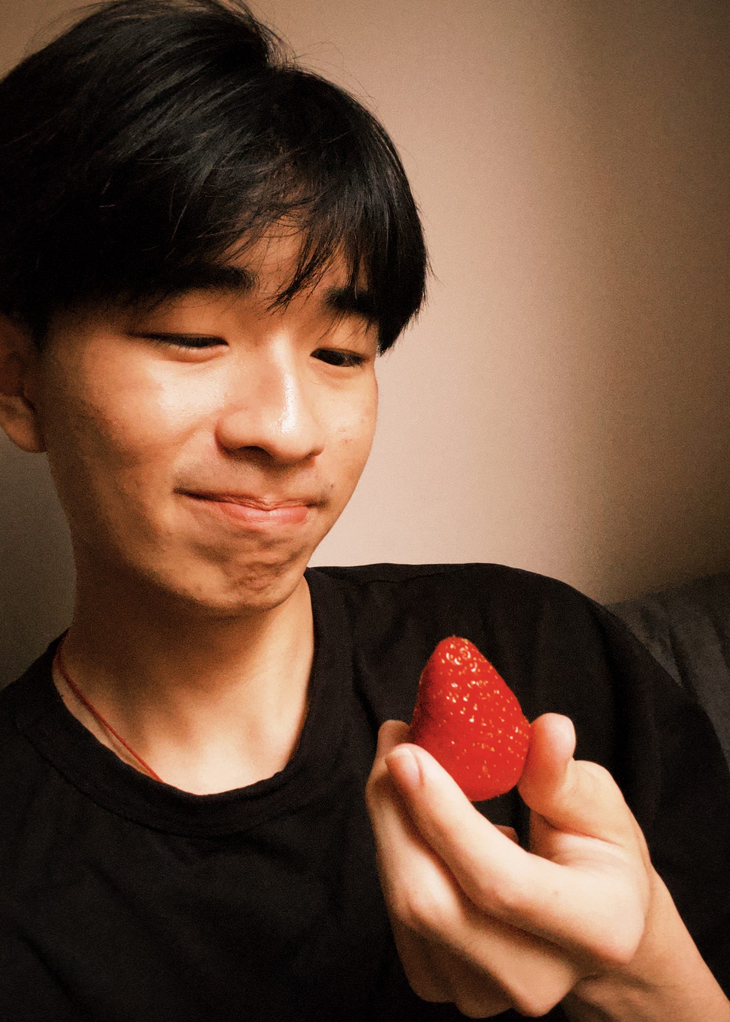 an asian young man holding a strawberry