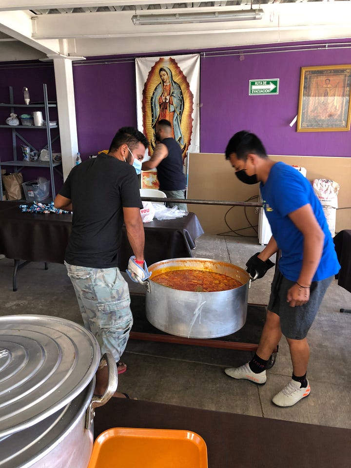 painting shows Jesus at last supper with migrants. Photo shows two men hauling a vat of stew at a migrant repite center.