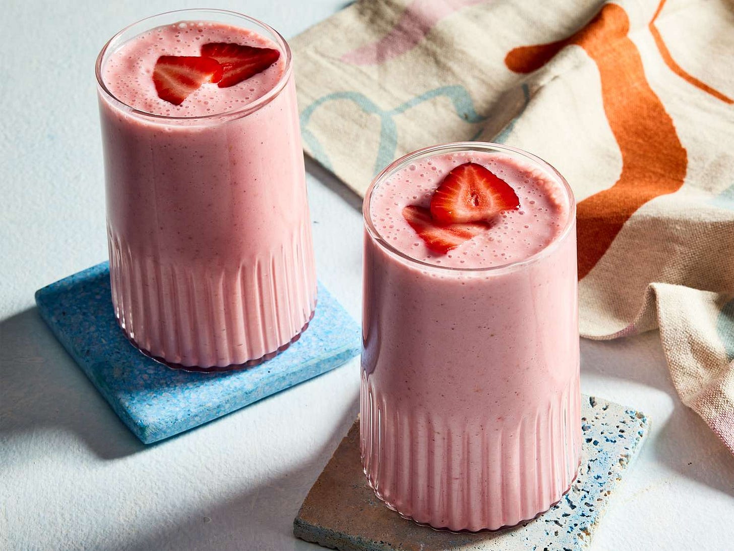 Two fruit and yogurt smoothies, served in tall glasses, topped with sliced strawberries