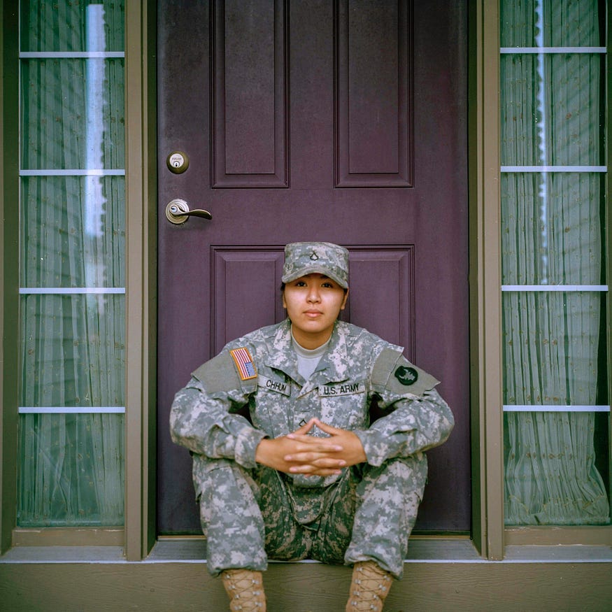 A female non-Caucasian member of the US Army, sitting in front of a purple door.