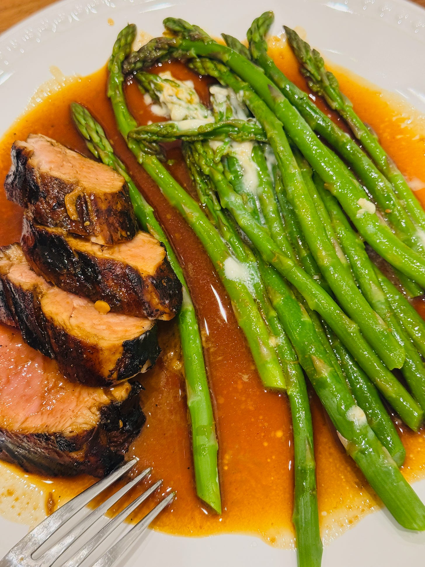 Pork tenderloin and asparagus on a while plate covered in marinade sauce. Pork tenderloin and asparagus on a while plate covered in marinade sauce.