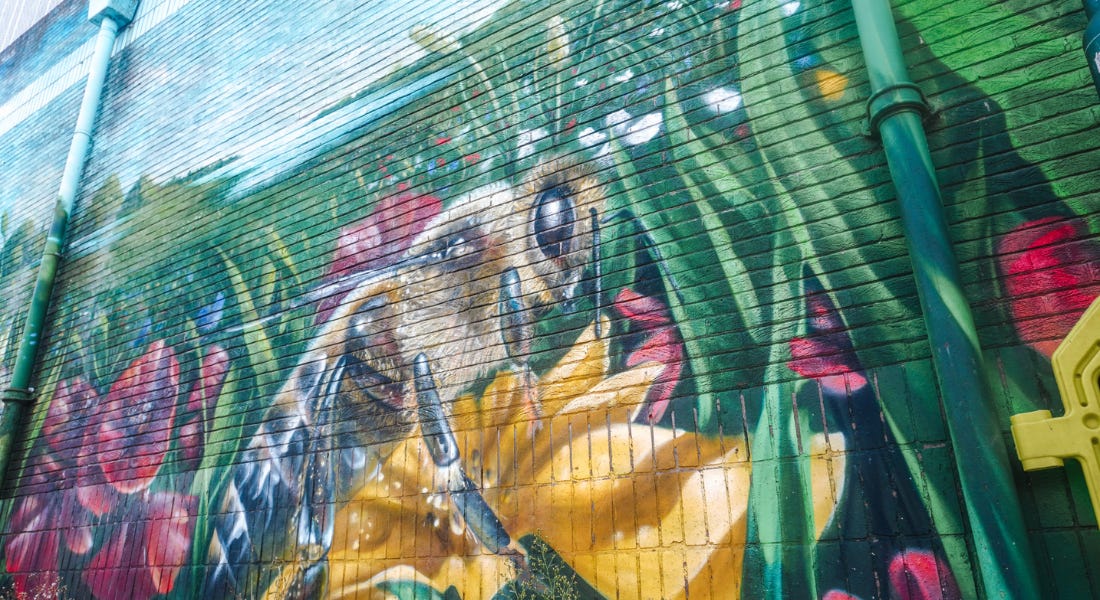 A mural with a bee on flowers with greenery around it A mural with a bee on flowers with greenery around it