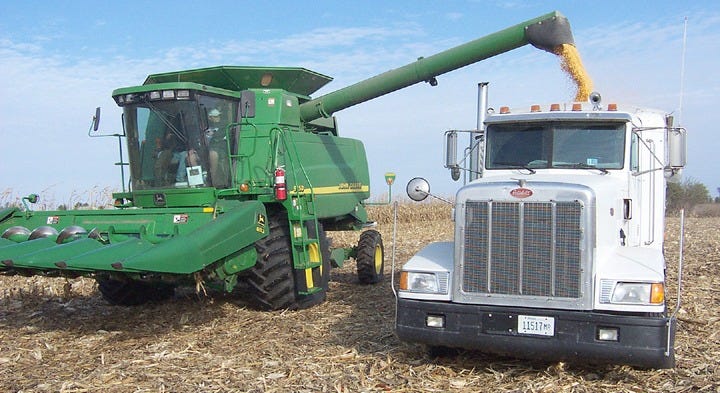 A farmer offloads corn from his combine into a semi trailer while working across a farm field. Two-way radios help coordinate this activity so trucks can load while combines continue picking crop in the field. | Photo from National Communications Magazine archives