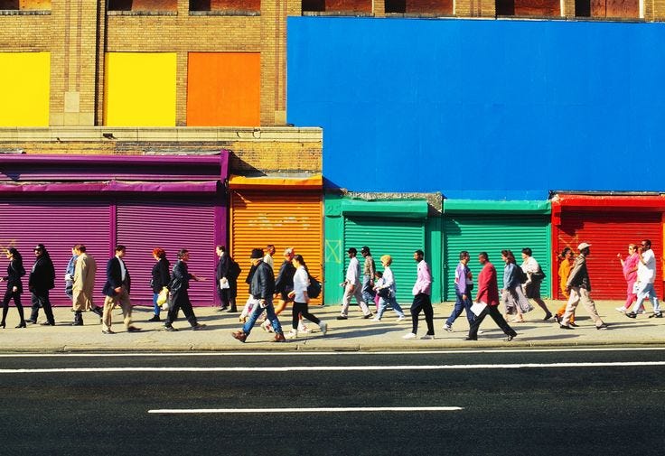 This may contain: a group of people walking down the street in front of some colorful shuttered buildings