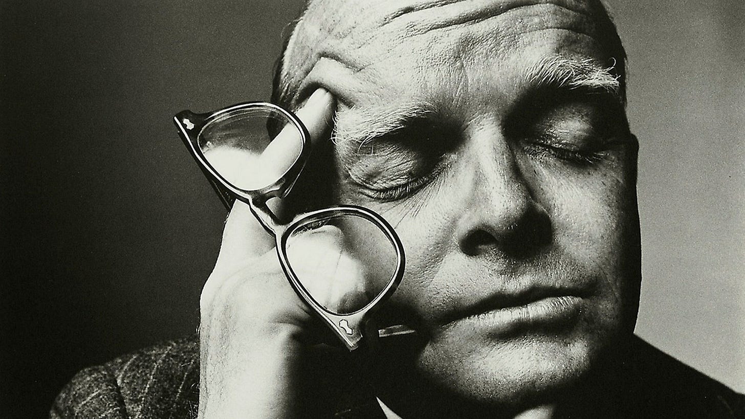 A photo of Truman Capote with his eyes closed, resting his head on his hand, which holds his glasses