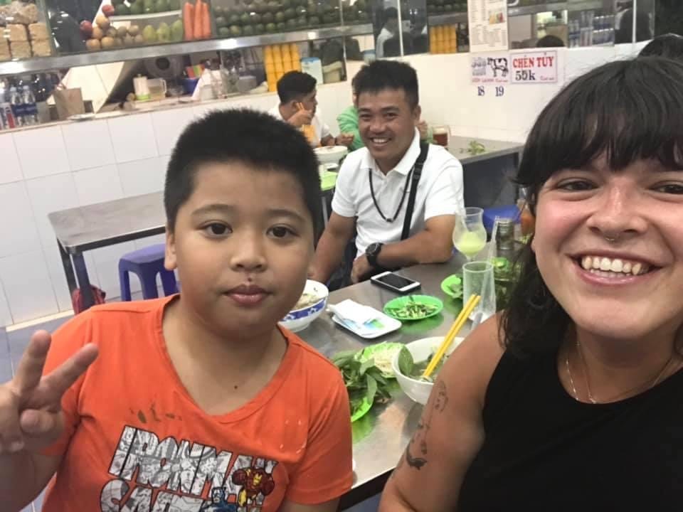 Lilii smiling with a man and his son holding up a peace sign at a restaurant in Vietnam.