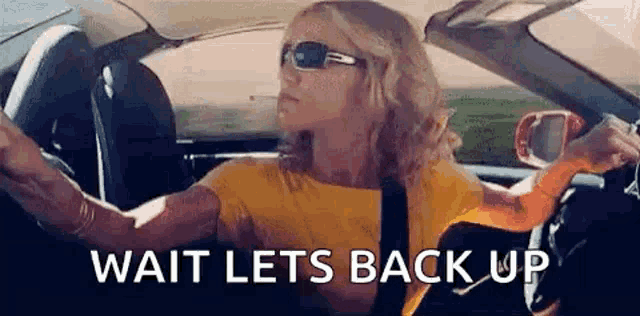 a woman is driving a car with the words `` wait lets back up '' written on the side .