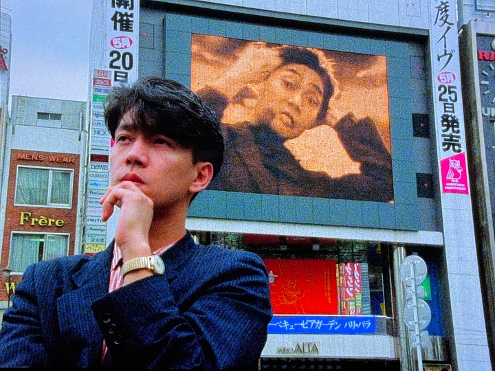 Still images from Tokyo Melody: Sakamoto in front of a large outdoor video screen, Sakamoto playing live in YMO.
