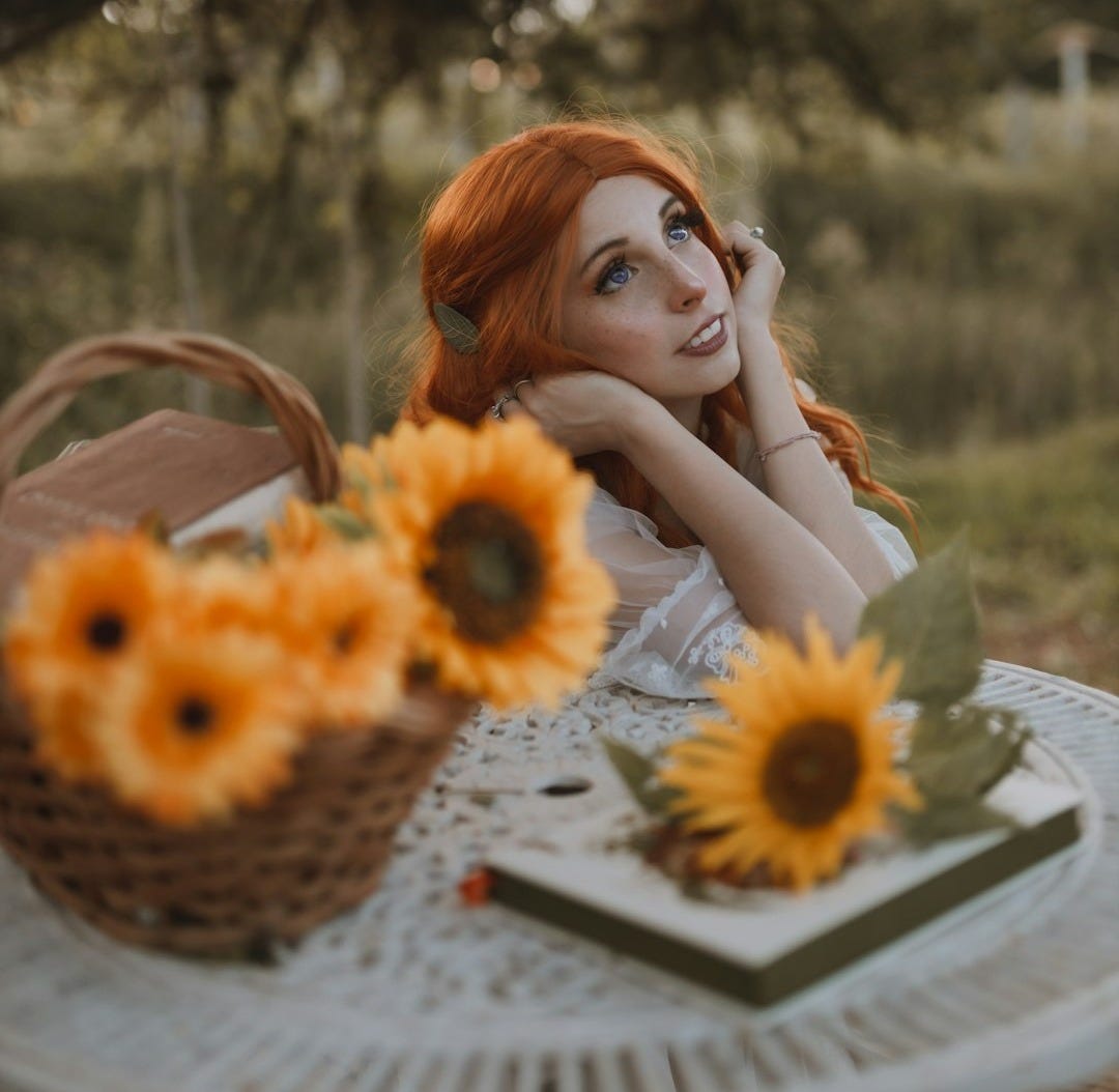 a woman sitting at a table with a basket of sunflowers a woman sitting at a table with a basket of sunflowers