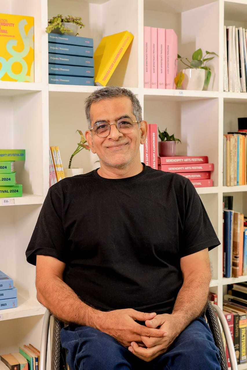 Salil Chaturvedi, an Indian man in blue jeans and black polo neck T-shirt is sitting in his wheelchair. Behind him is a bookshelf full of colour coded books. Salil Chaturvedi, an Indian man in blue jeans and black polo neck T-shirt is sitting in his wheelchair. Behind him is a bookshelf full of colour coded books.