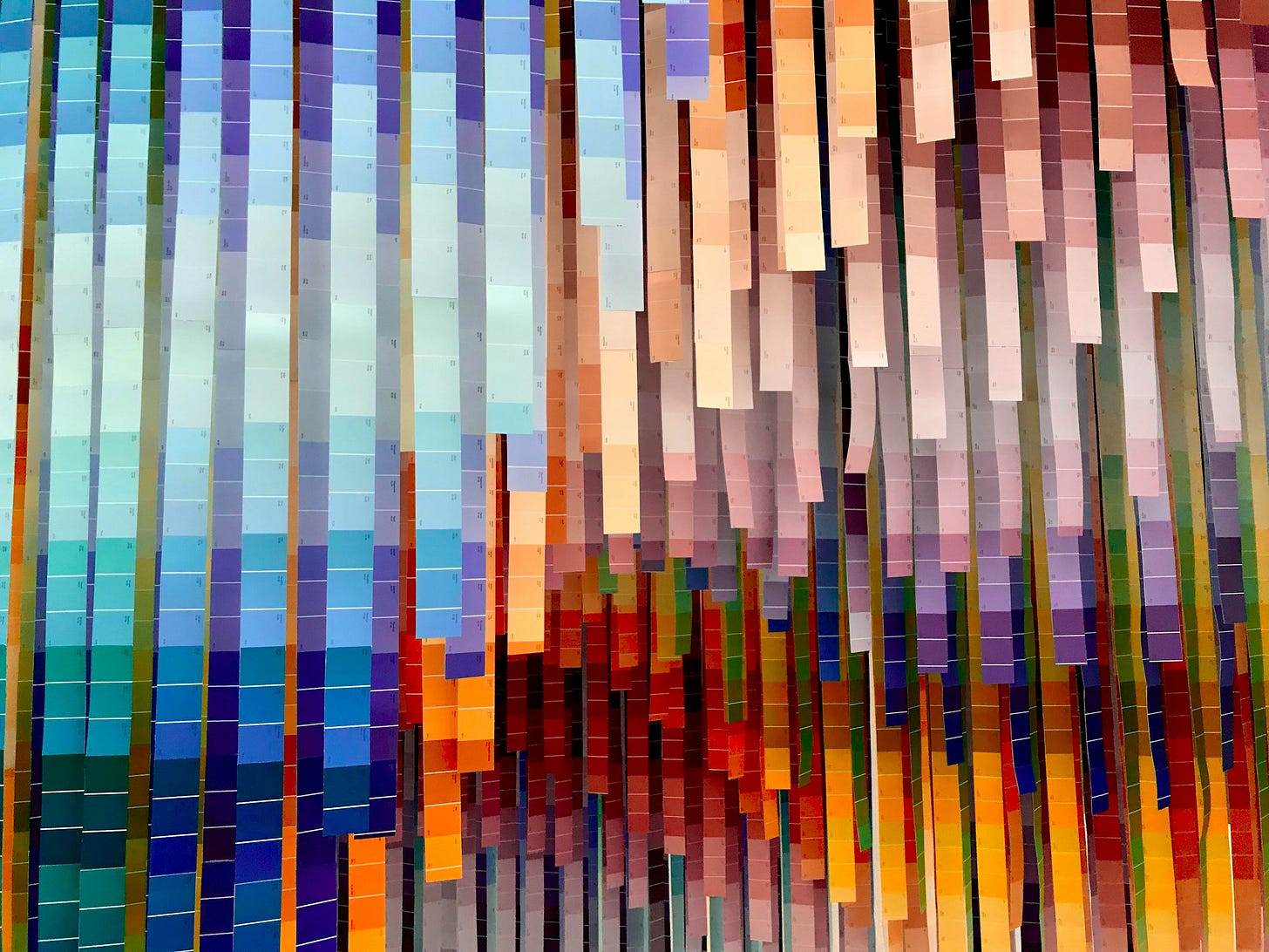 Una serie di fettuccine di carta colorate che pendono dall'alto, ciascuna con diverse tonalità di un colore.