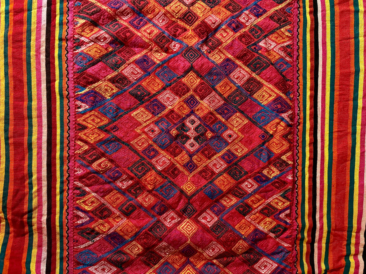 Colourful hand-embroidered textile, angular swirls and diamond shapes.