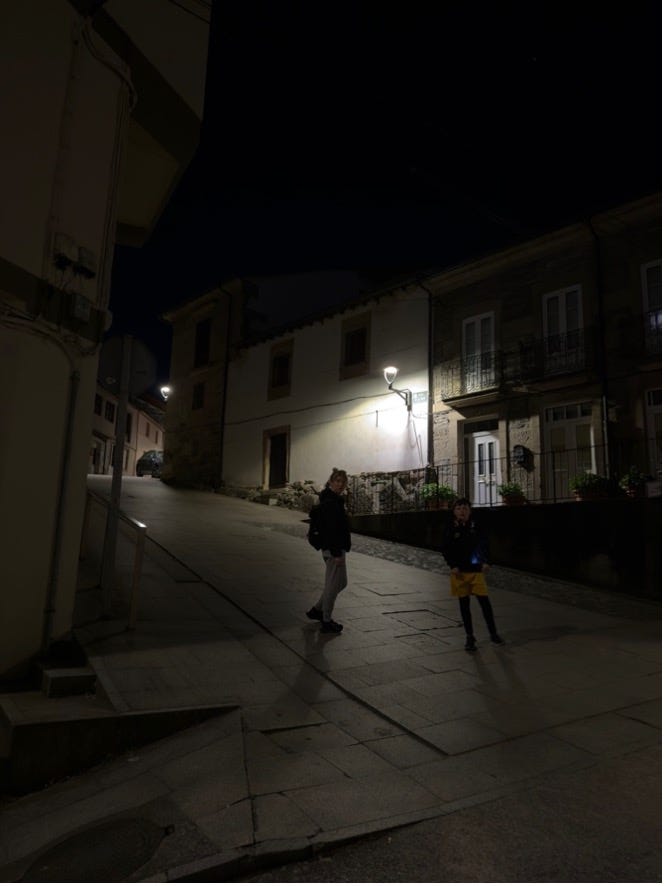 Two people standing in shadow on a steep street surrounded by buildings.