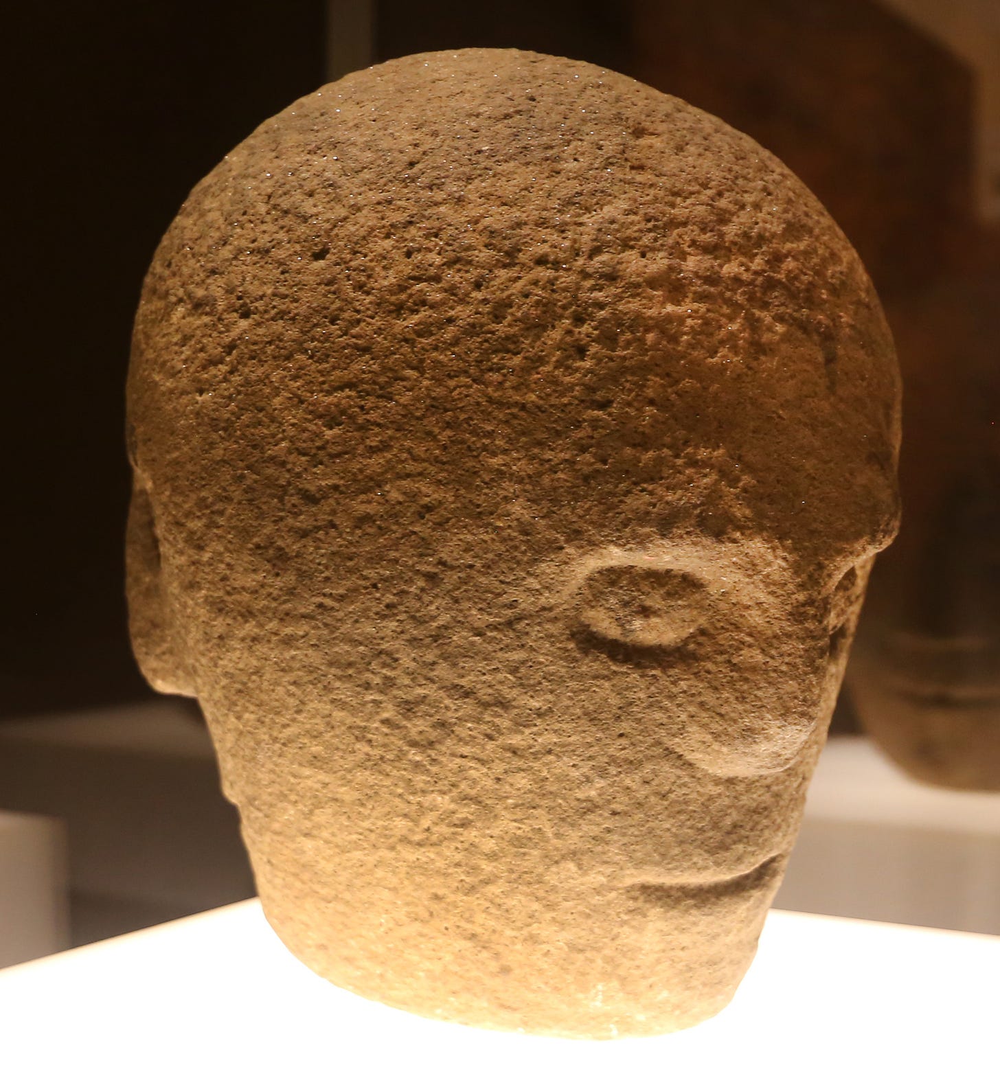 a sandstone head carved with multiple features is lit from below and appears spooky