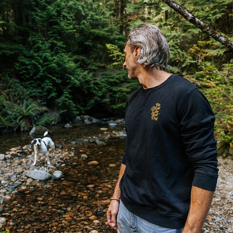 awkward man frolics around stream with dogs wearing very nice merch from be more like your dog