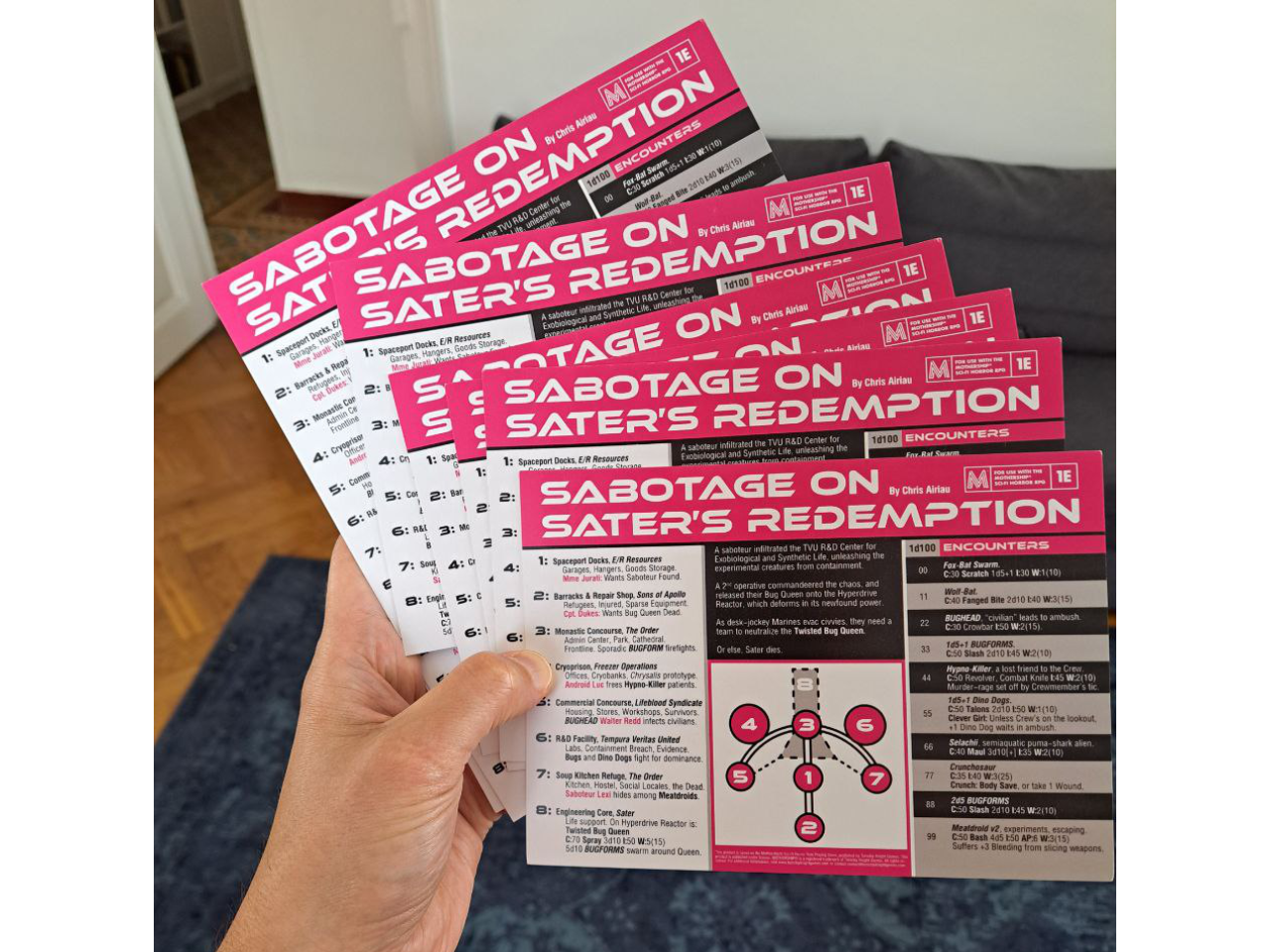 I’m holding a stack of pink, black and white 5 × 7 inch postcards that read “Sabotage on Sater’s Redemption for Mothership RPG 1E” across the top.