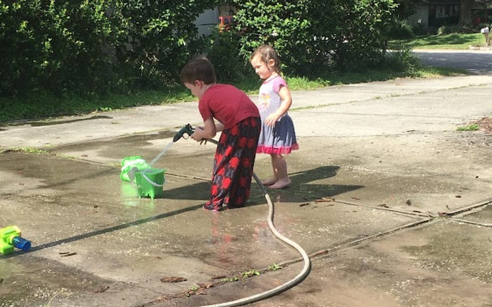 Photo of two of the author’s young children playing with a hose and bucket of water on a driveway.