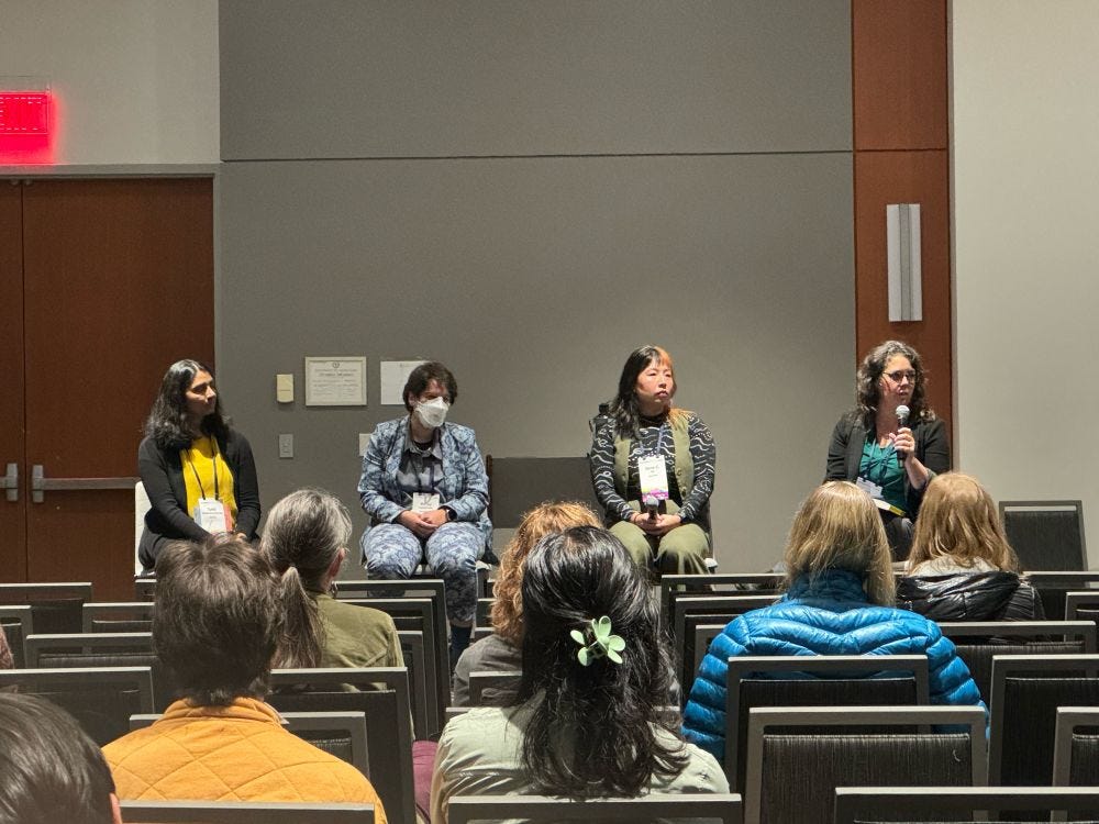 Four panelists sit on stools in a conference room