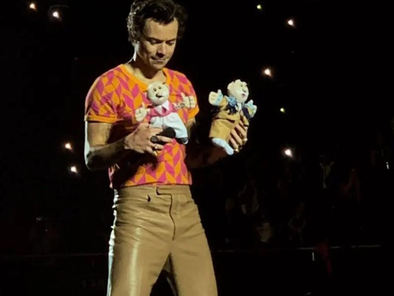 Harry Styles con playera naranja con peluches de Dr. Simi en manos