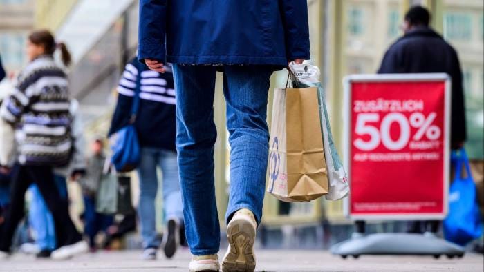 A shopper carries a bag past a sign advertising an ‘Extra 50 percent discount on already discounted  items’ outside a clothing retail store in Berlin 