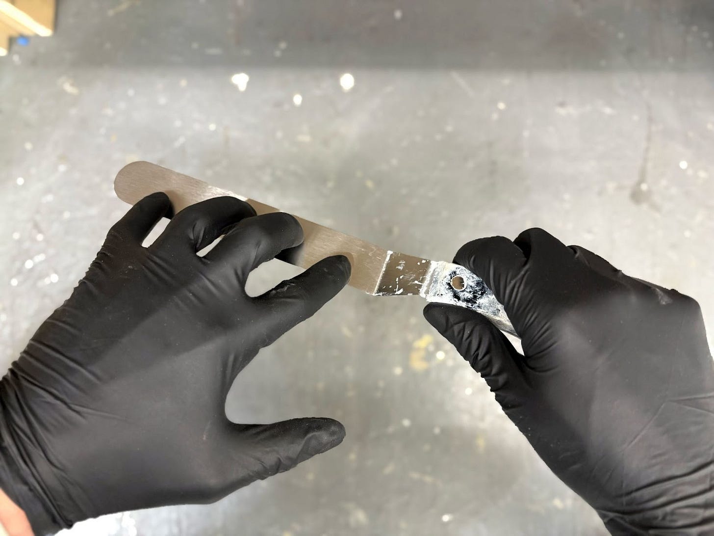 Two hands in black nitrile gloves hold a palette knife to achieve the technique described.