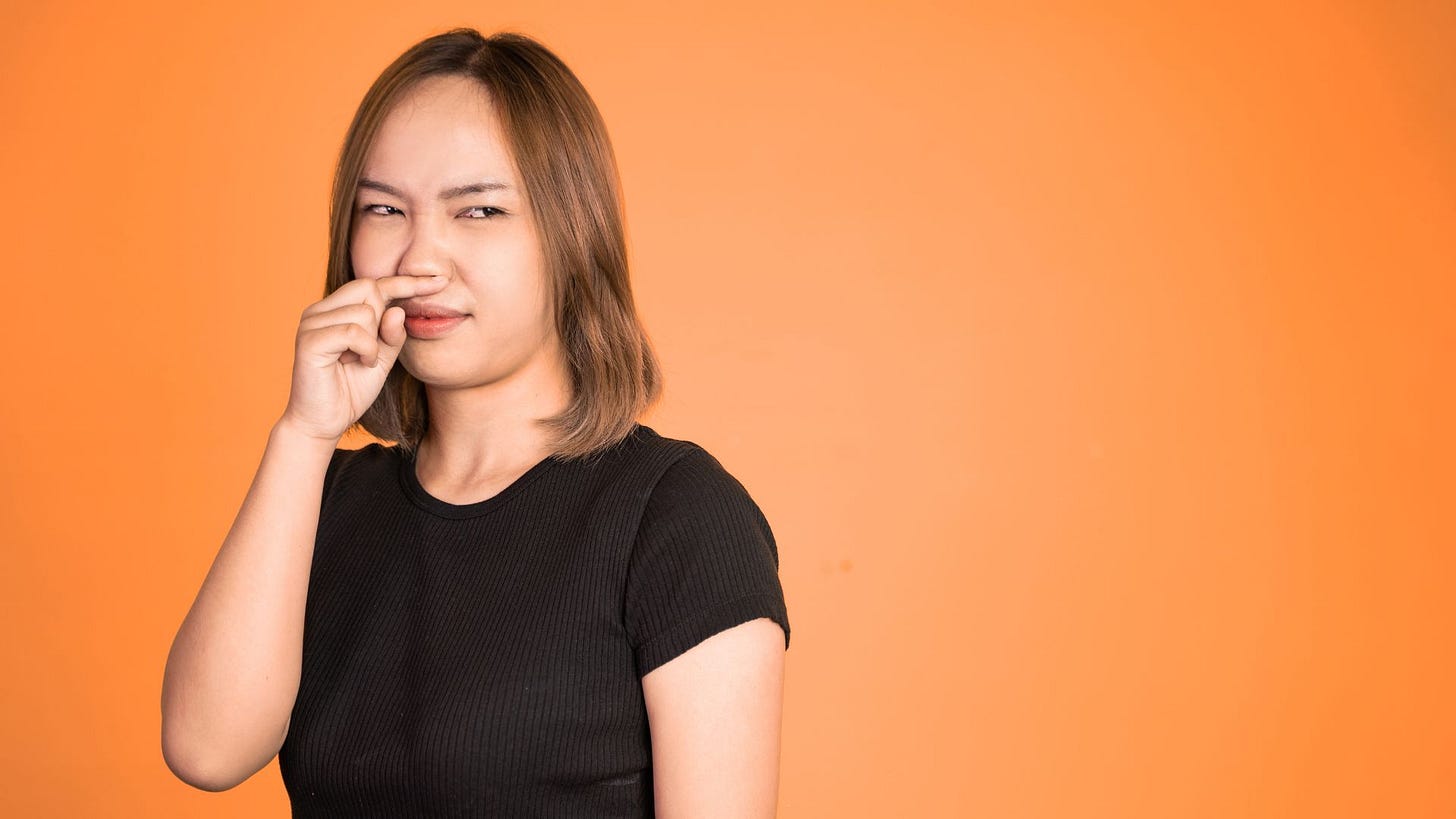 Woman holding a finger under her nose with an expression of digust