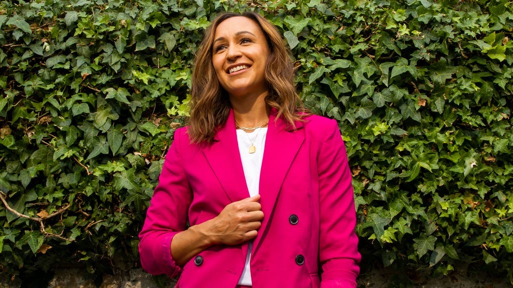 A portrait shot of Jessica Ennis-Hill wearing a hot pink trouser suit, standing in front of a wall covered in green ivy A portrait shot of Jessica Ennis-Hill wearing a hot pink trouser suit, standing in front of a wall covered in green ivy