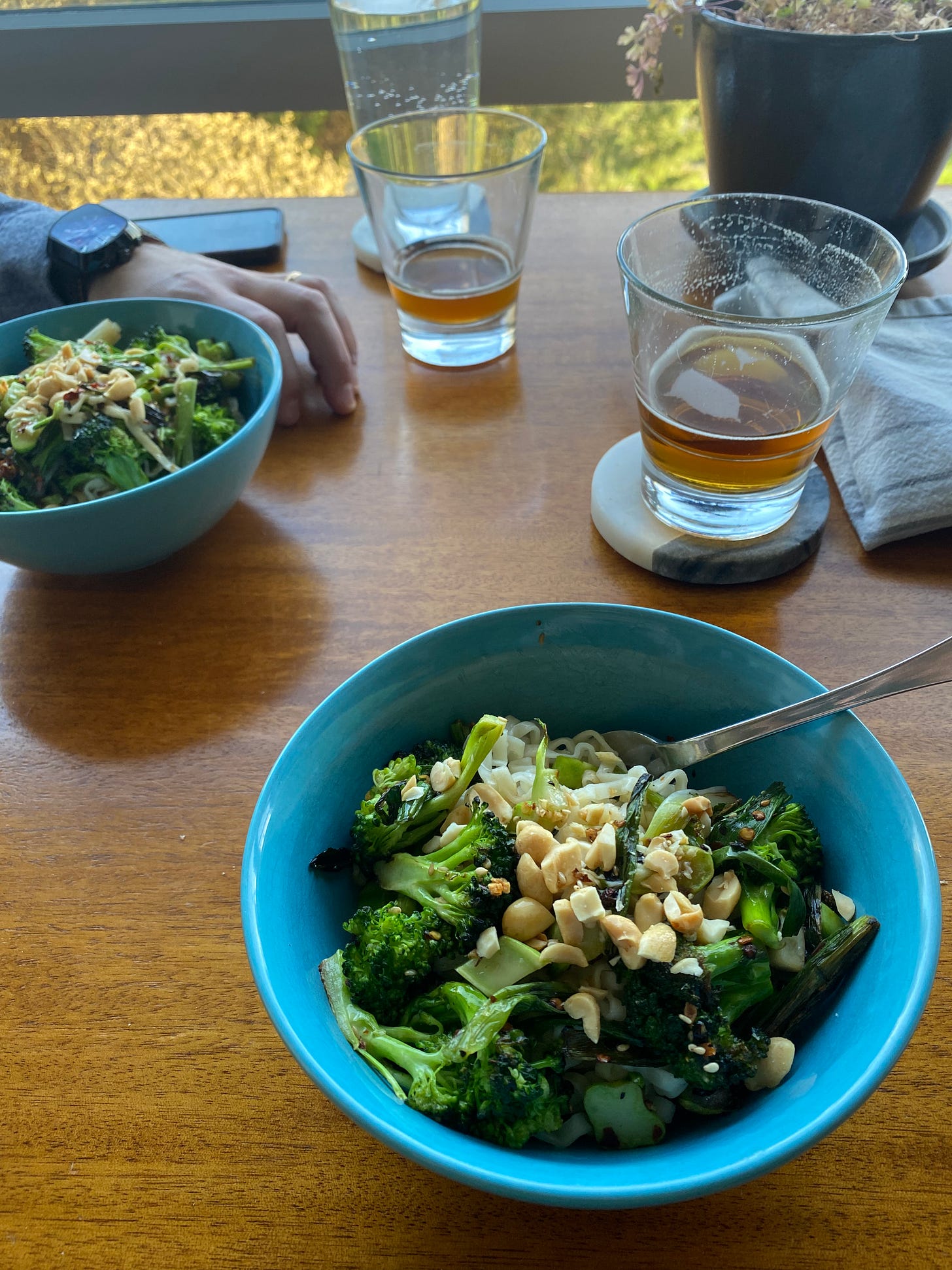 Two blue bowls of noodles in chili oil, topped with sautéed broccoli and bok choy, and chopped peanuts.