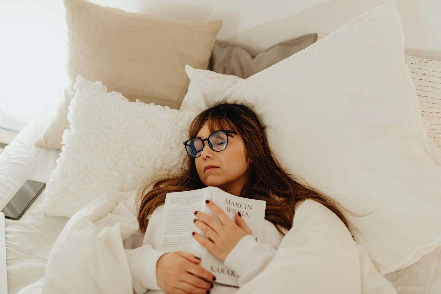 Women wearing glasses sleeping on her bed clutching a book to her chest